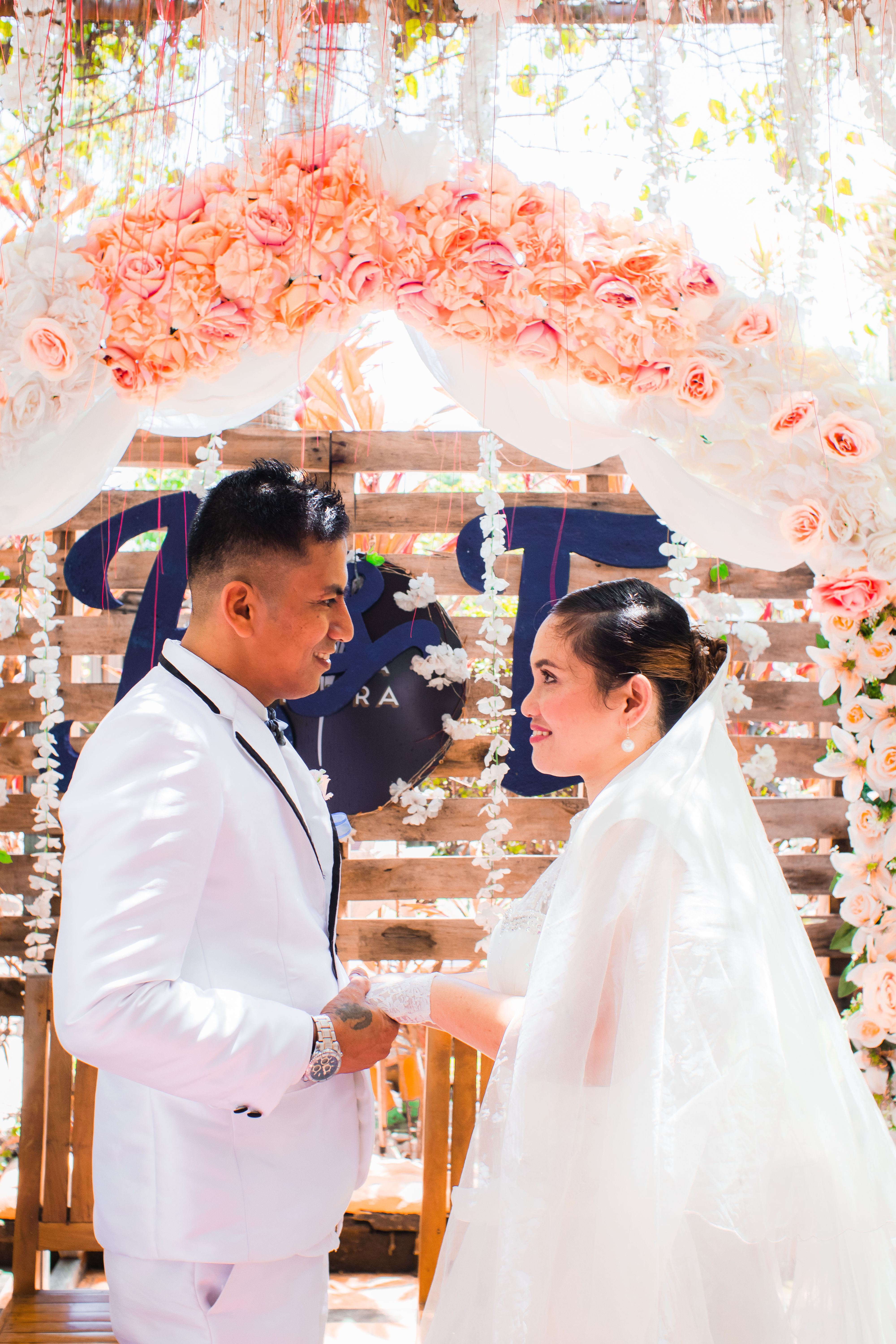 A lovely outdoor wedding ceremony featuring a couple under a floral arch holding hands.