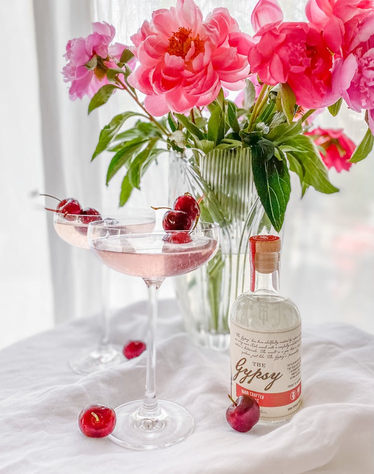 Cocktail In Martini Glass With Cherries Next To Pink Flowers In Vase