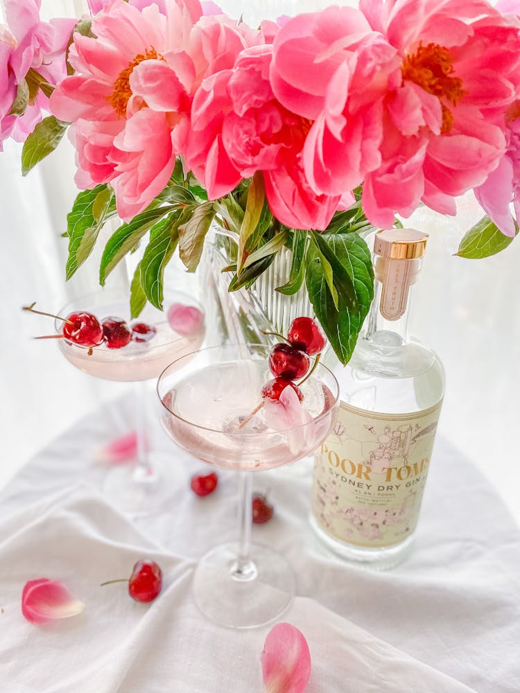 Cocktail In Martini Glass With Cherries Next To Pink Flowers In Vase