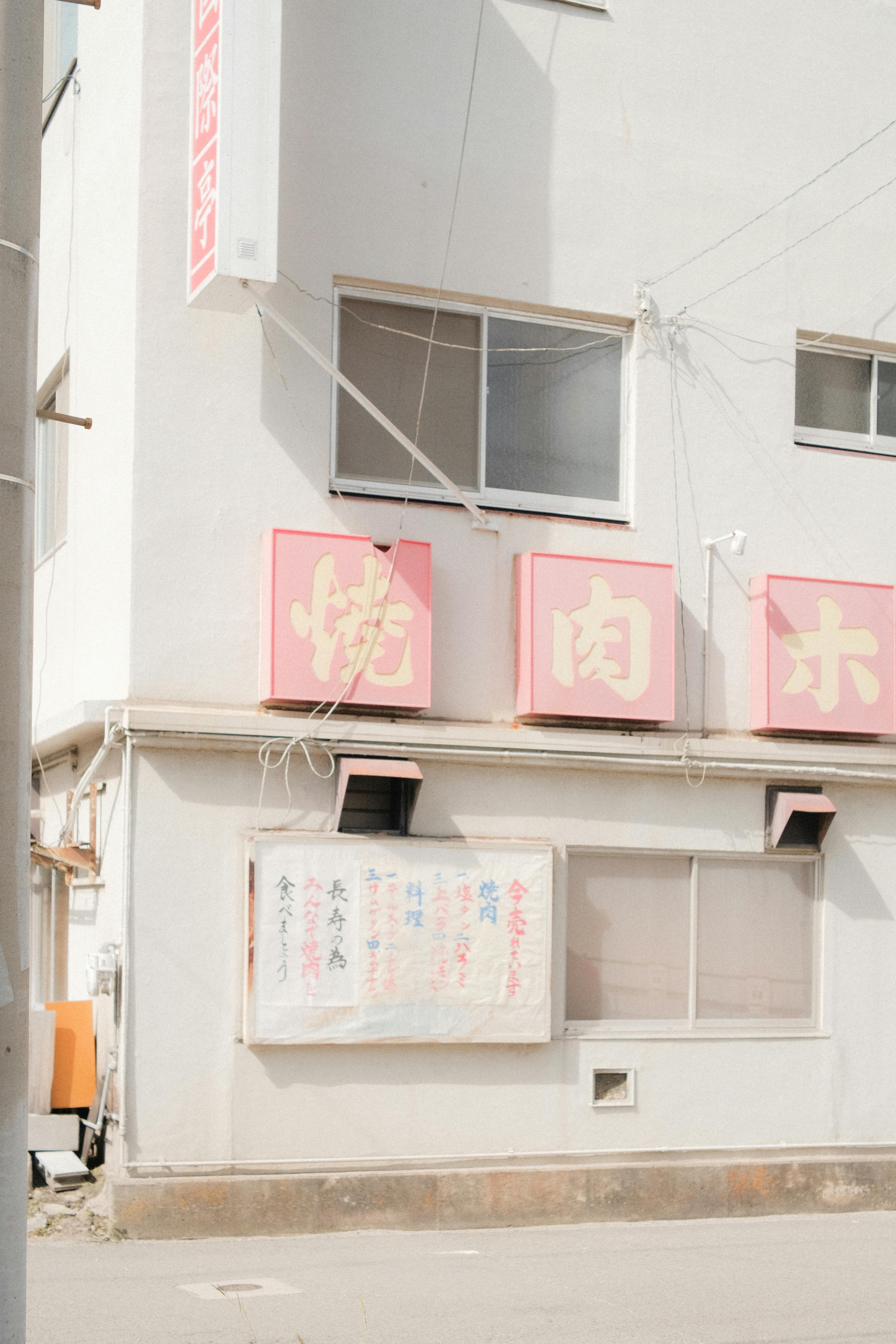 A beige urban building's facade with Asian signage, concrete structures, and natural light.