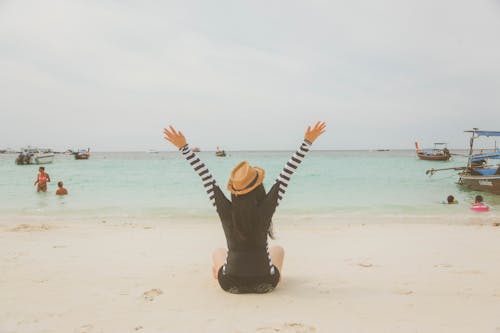 бесплатная Женщина, сидящая на пляже возле лодок и людей в течение дня Стоковое фото