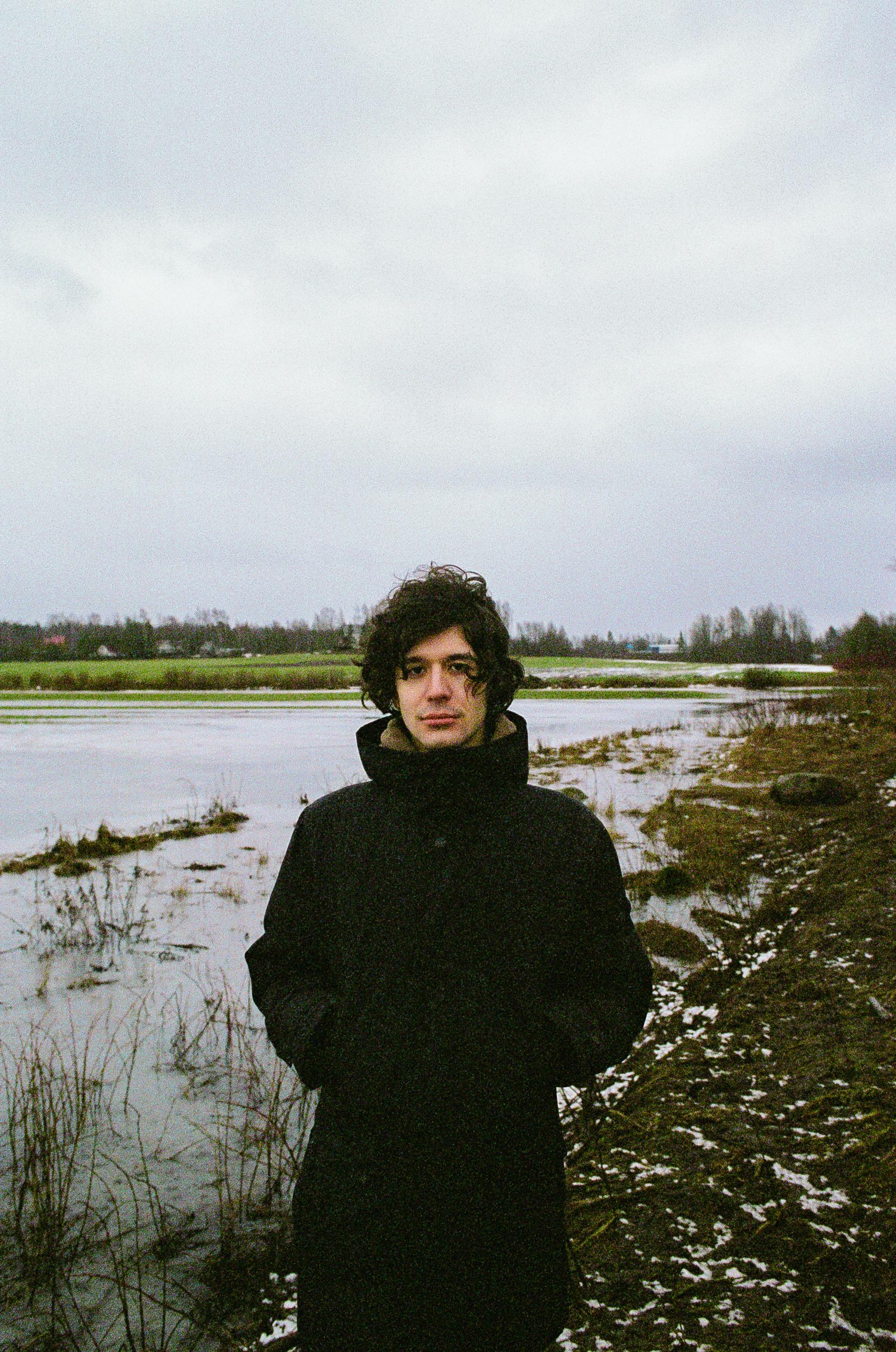 Man in a black coat standing by a snowy water's edge in Saint Petersburg during winter.