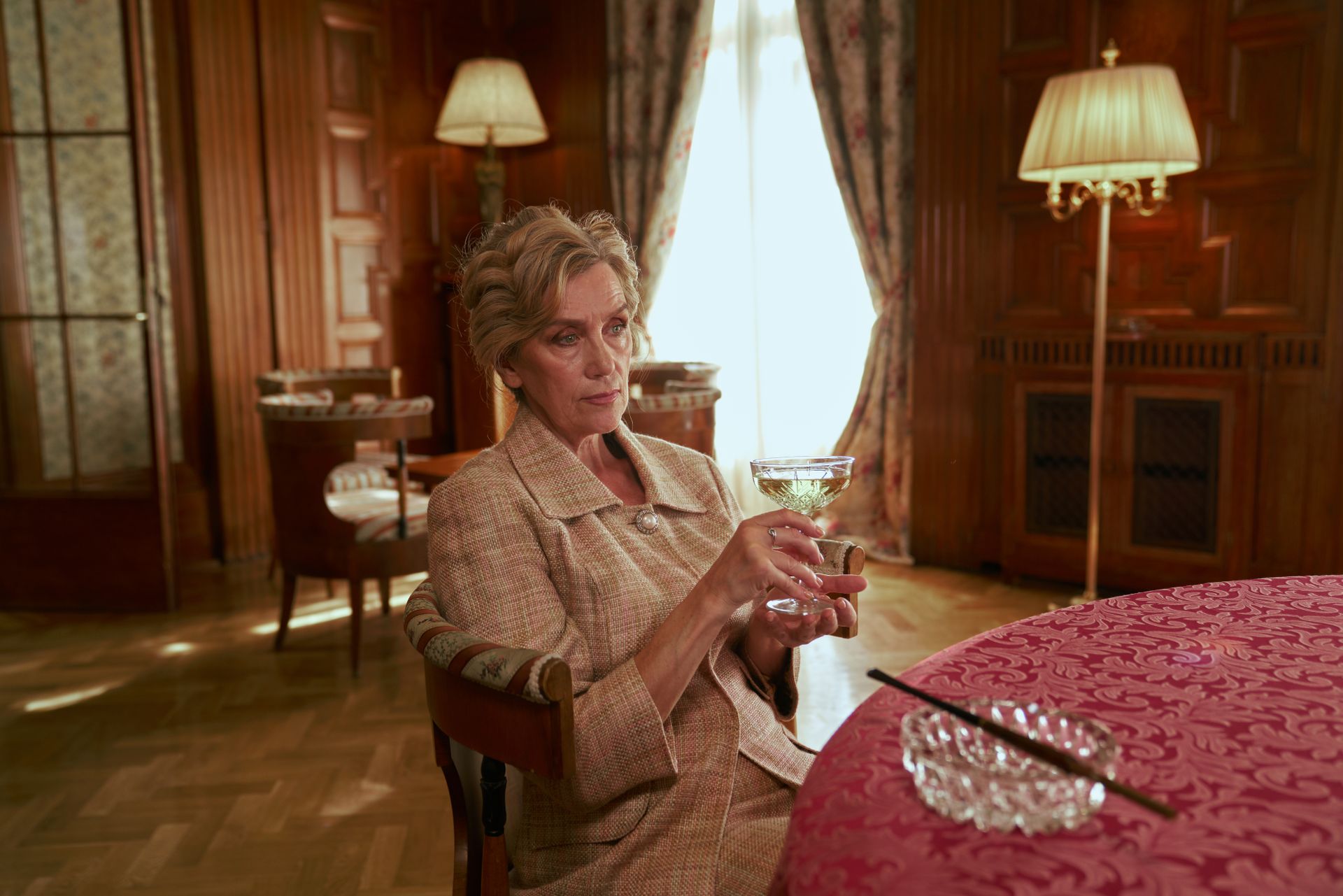 A senior woman holds a wine glass in a vintage luxurious interior, reflecting elegance.