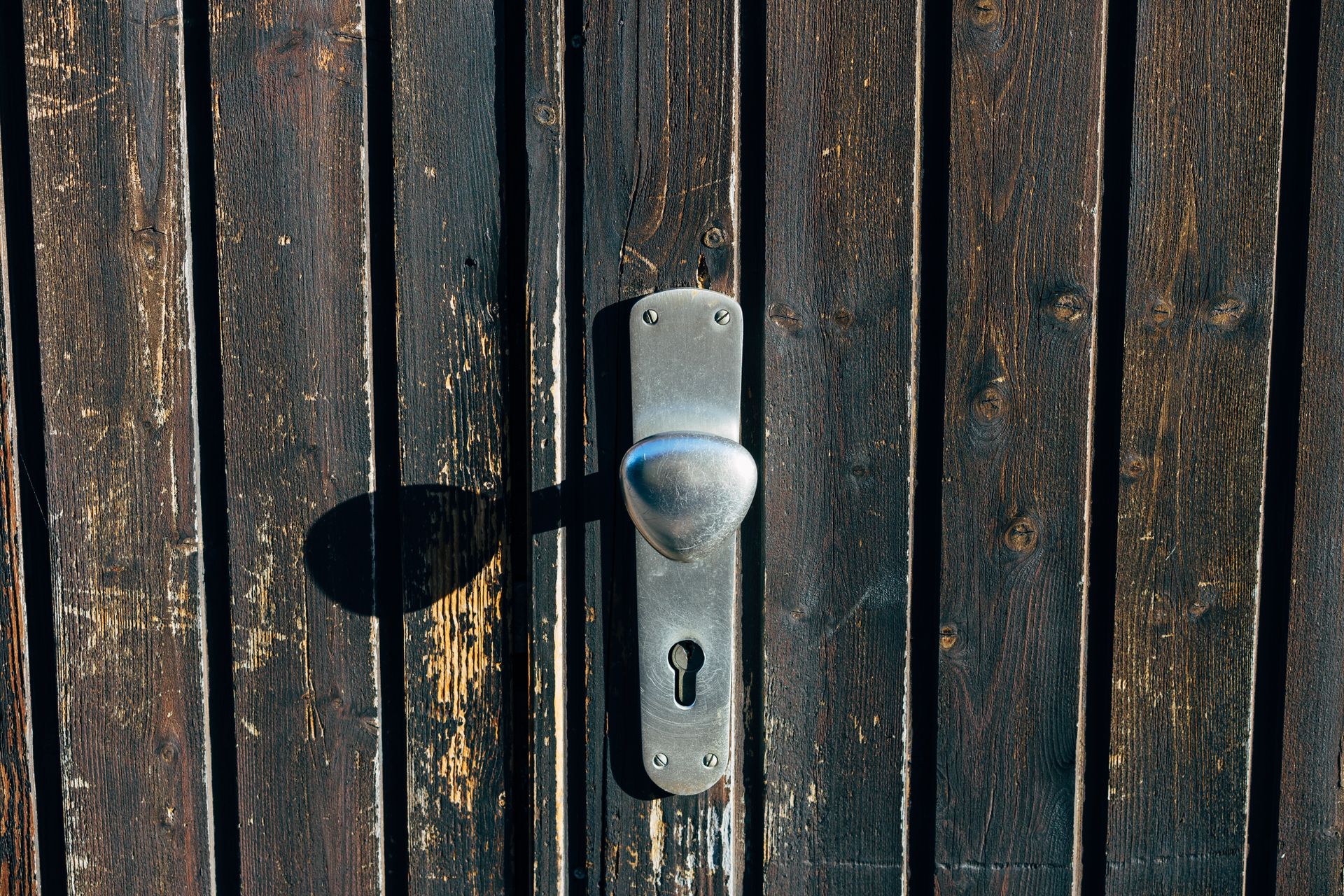 Detailed close-up of a metallic door knob and keyhole on a textured wooden door with natural light.