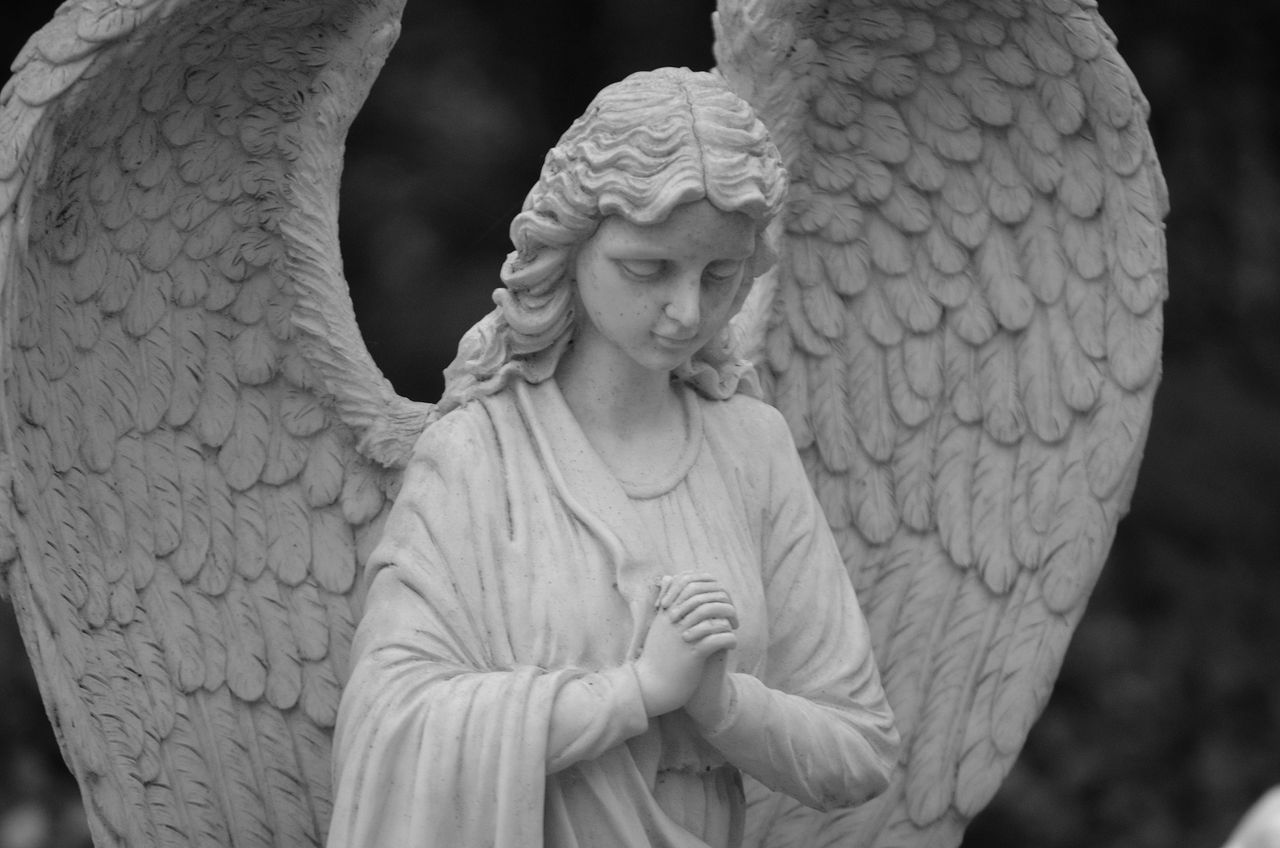 a grayscale close up of a serene angel statue with wings and praying h