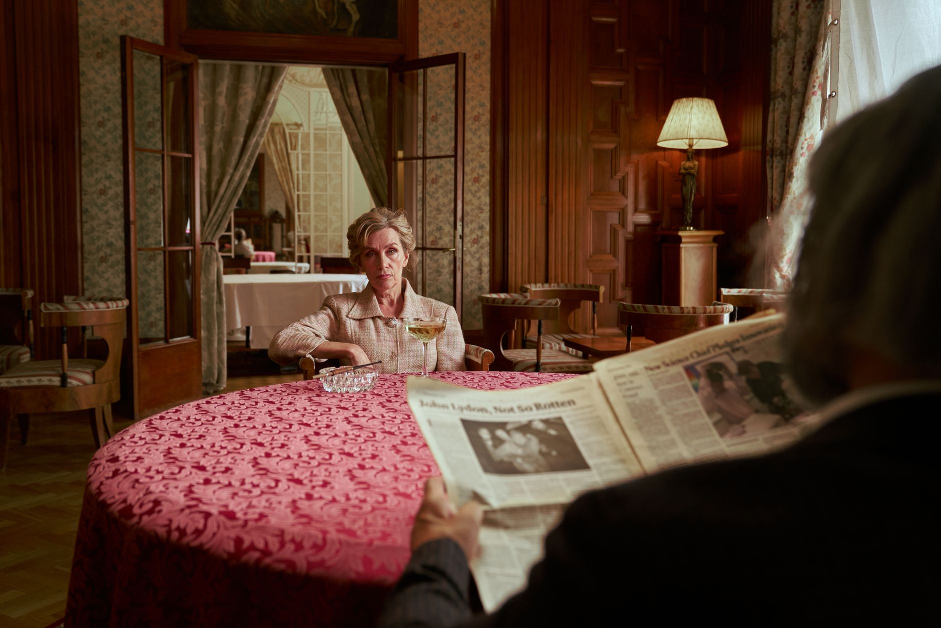 A senior couple enjoys a quiet moment with a newspaper in a vintage, luxurious living room.