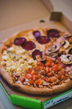 Enjoy a delicious four seasons pizza featuring toppings like mushrooms and tomatoes in a convenient takeaway box.