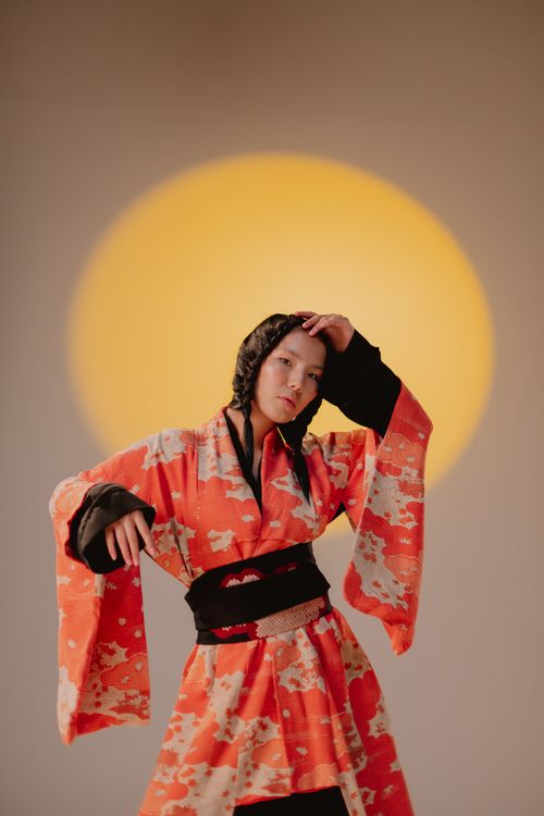 Free Captivating portrait of a woman in a vibrant kimono with a warm backdrop. Stock Photo
