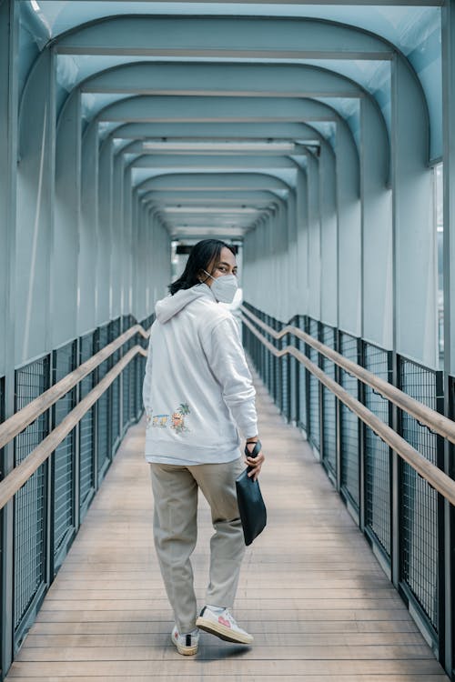 Back View of a Man Wearing a White Hoodie Walking on the Wooden Platform