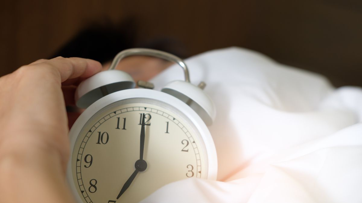 Person holding an alarm clock set for an early morning departure