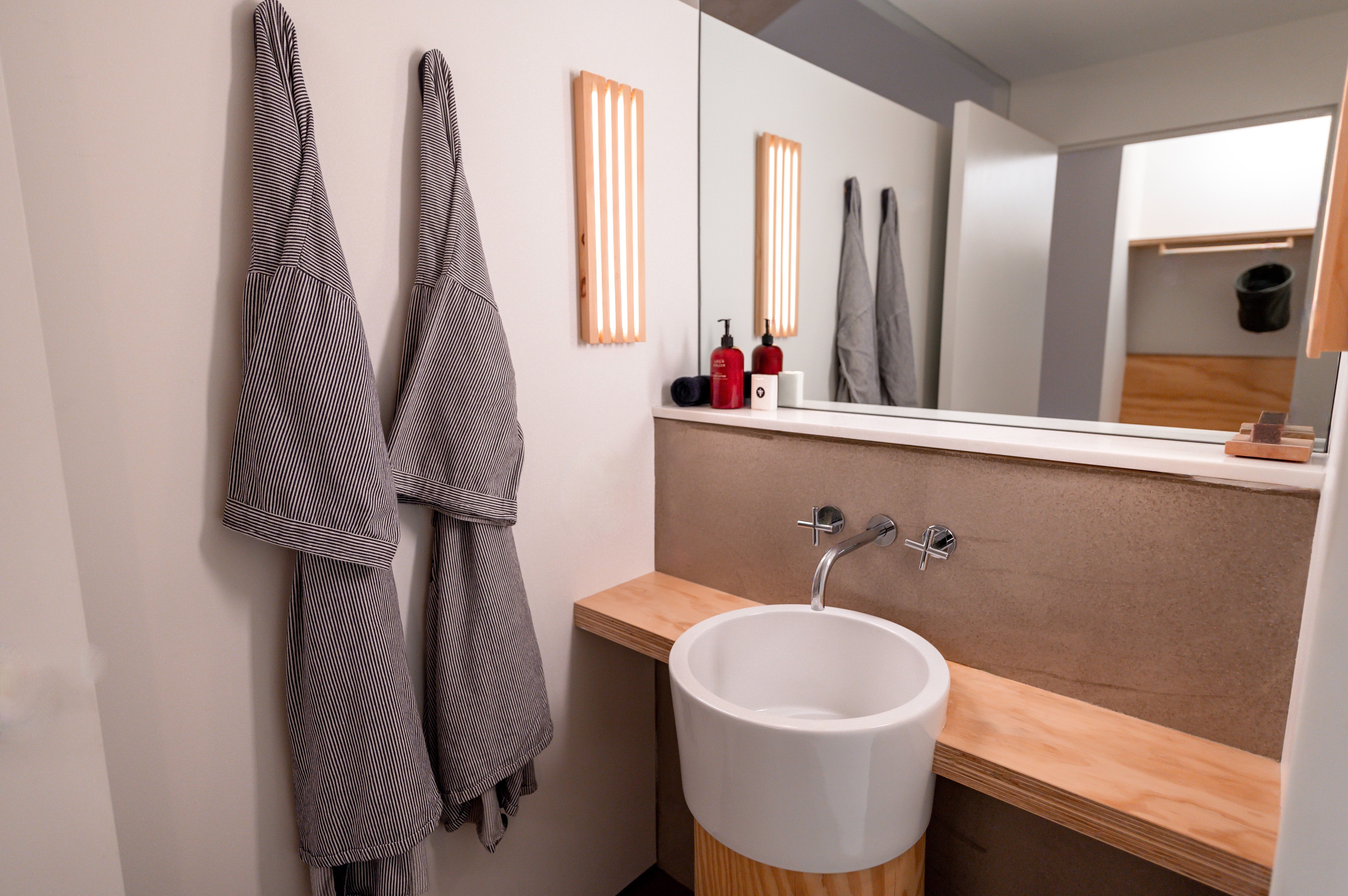 A sleek, minimalist bathroom with a round sink, wooden countertop, and hanging bathrobes.