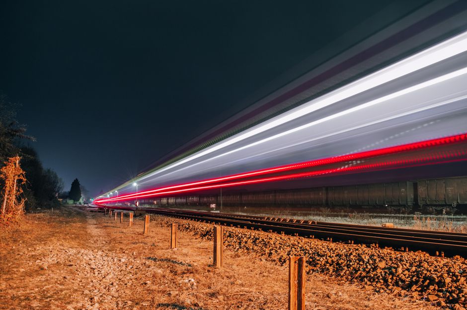 Long exposure of a train creating vivid light trails on a nighttime railway track.