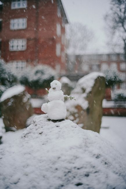 Charming snowman perched on a snowy surface with urban buildings in the background.