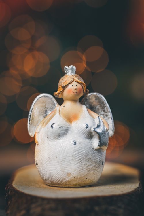 Free Cute angel figurine with wings and festive bokeh lights, perfect for holiday decoration. Stock Photo
