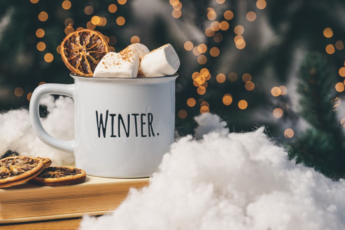 Warm winter mug with marshmallows and dried oranges, surrounded by festive lights and snow cotton.