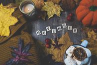 Warm autumn still life featuring a candle, pumpkin, leaves, and hot drink for November ambiance.