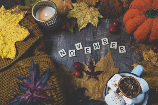 Warm autumn still life featuring a candle, pumpkin, leaves, and hot drink for November ambiance.