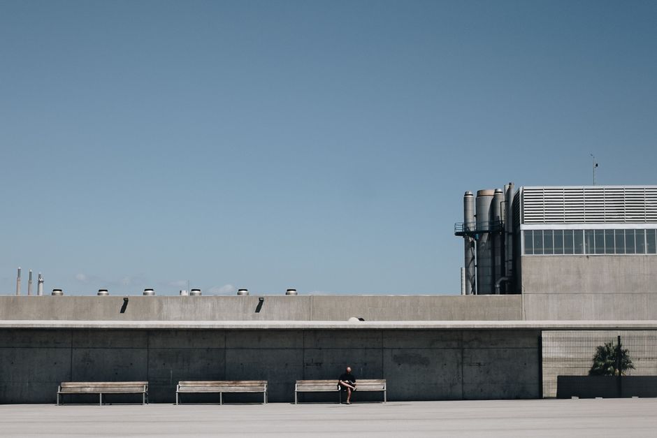 A person sitting by a modern industrial building in Barcelona under a clear sky.