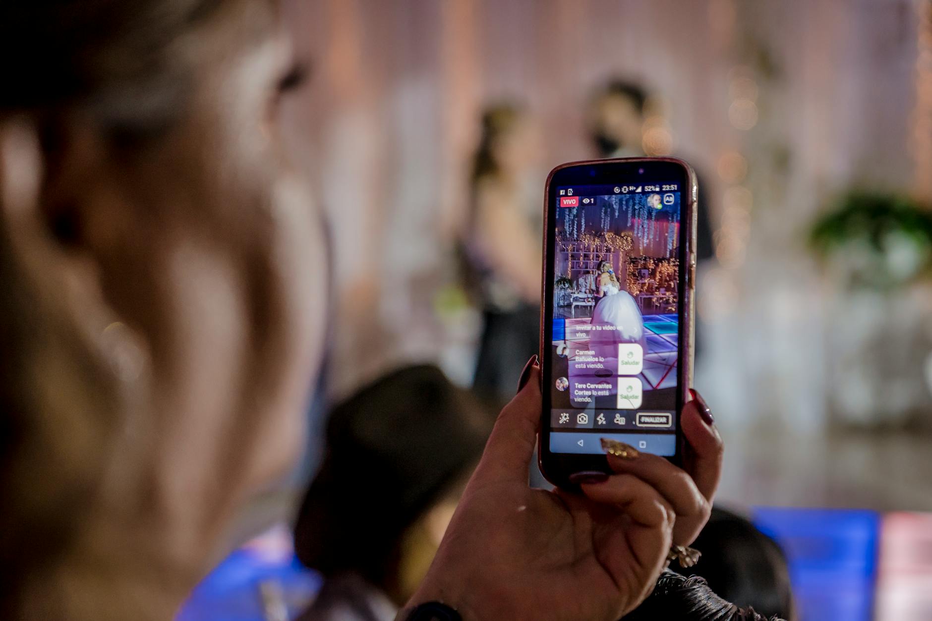 A woman captures a live event video using a smartphone at a lively indoor gathering.