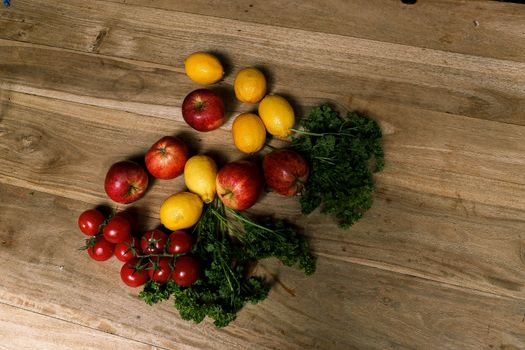 Top view of fresh apples, lemons, tomatoes, and parsley on wooden surface.