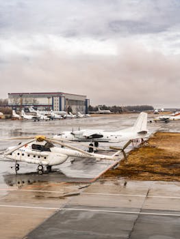 Planes and helicopters parked on a tarmac of a rainy airport. Overcast skies enhance the industrial atmosphere.