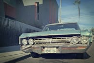 一辆明显磨损的经典古董车停在城市街道上，前方是晴朗的天空