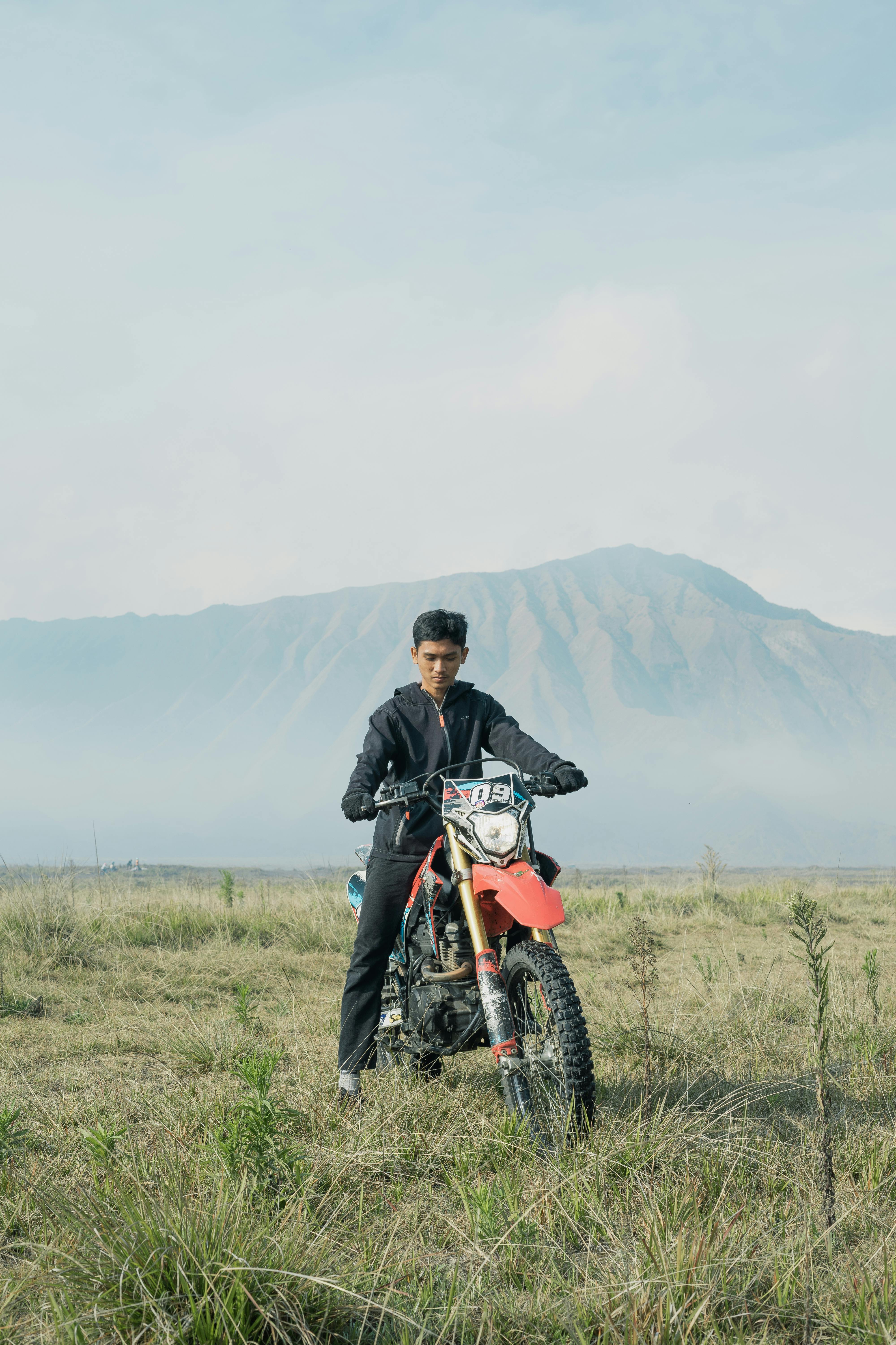 Man on motocross bike in East Java's scenic landscape with mountains and fog.