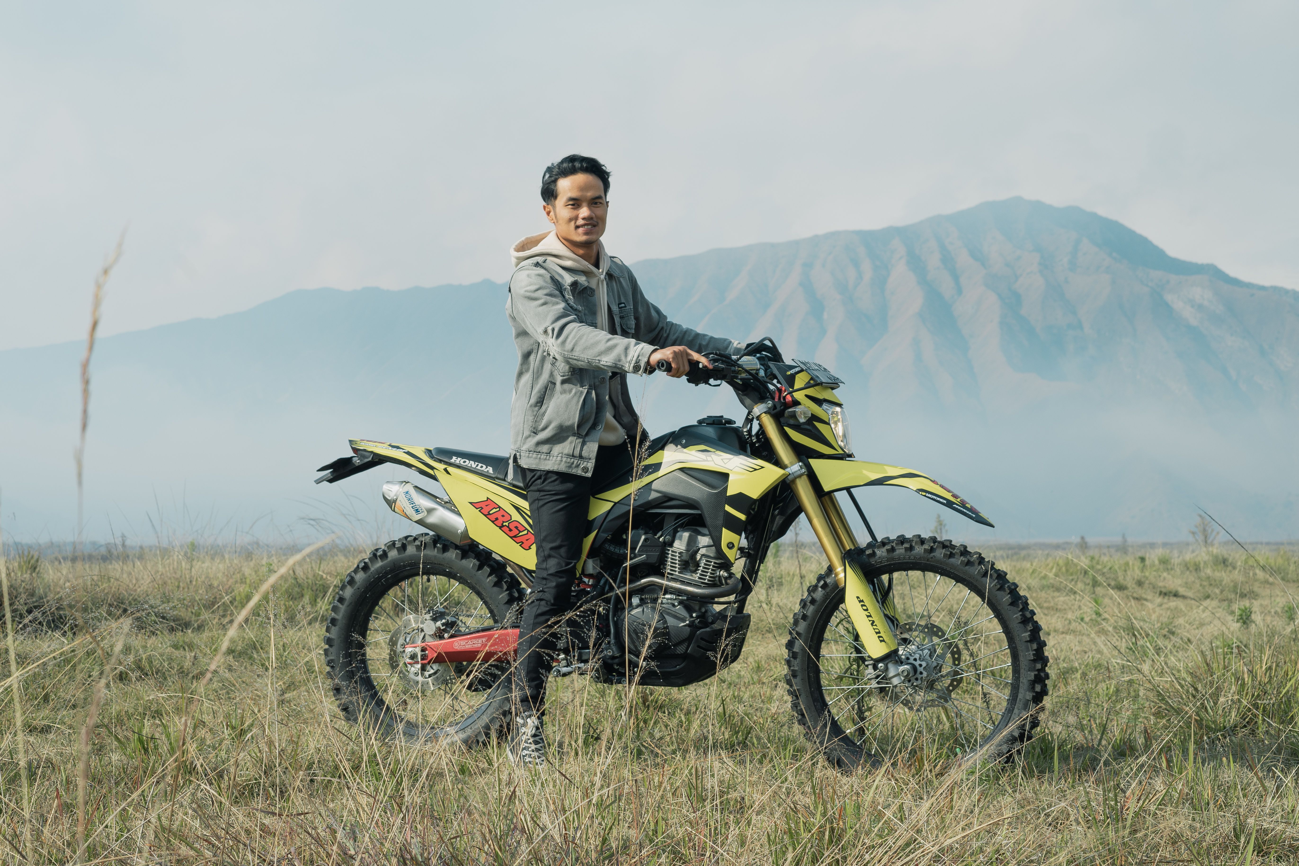A man on a yellow dirt bike amidst East Java's scenic mountains, exuding adventure.