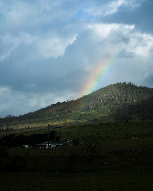 Rainbow Over Green Mountain Under Cloudy Sky