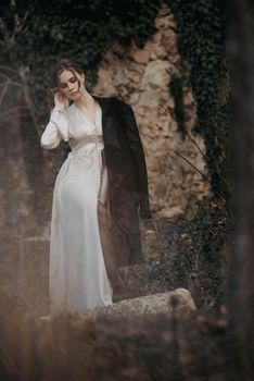 Stylish woman in a white dress poses gracefully outdoors with natural rock background.