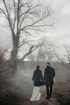 A couple elegantly strolling through a misty forest path, wearing black coats.