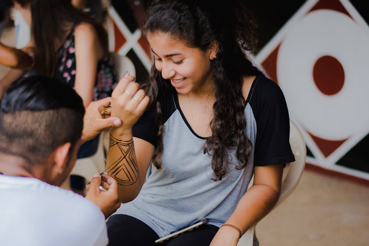 Girl With Black Curly Hair Getting Hand Painted By A Brunette Man