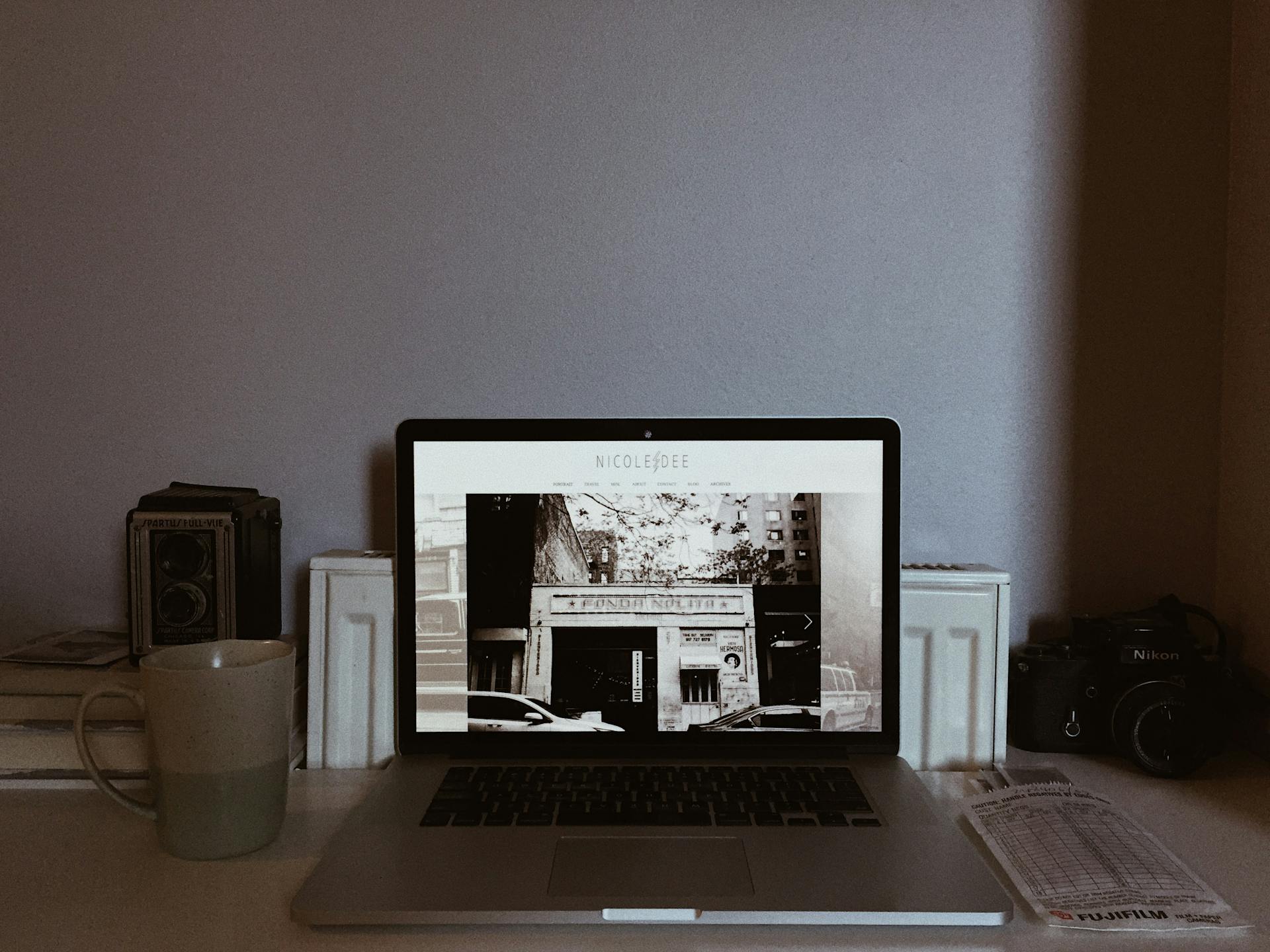 A cozy home office setup with a laptop, vintage camera, and mug, perfect for remote work.