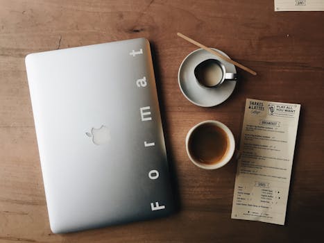 Flat lay of a laptop, coffee cups, and restaurant menu on a wooden desk setting the scene for a tech-savvy workspace.