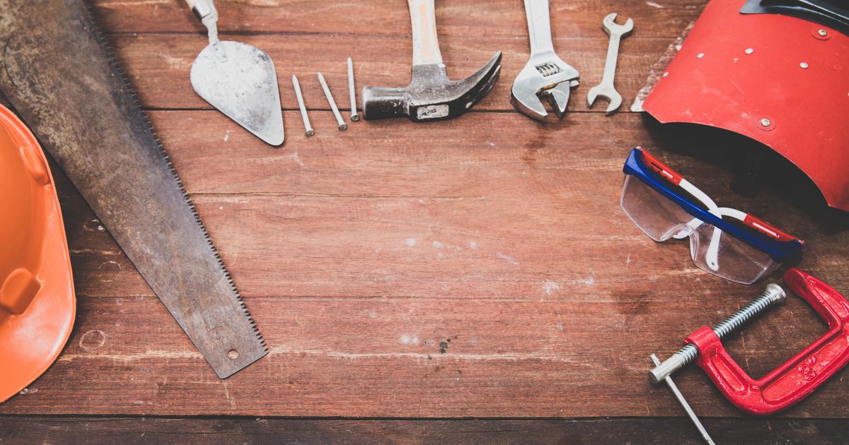 An organized flat lay of hand tools including a hammer, saw, and wrenches on a rustic wooden surface