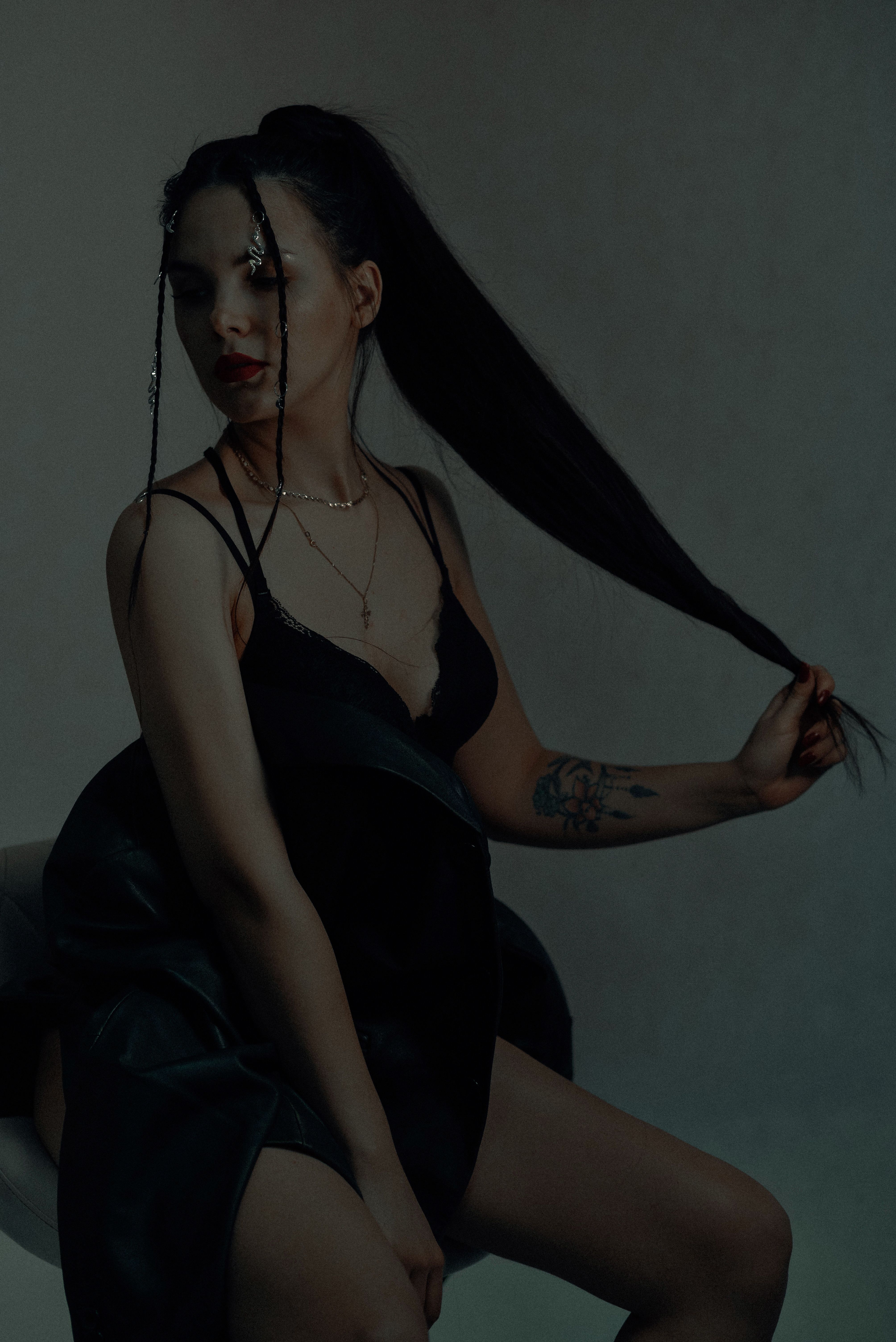 Elegant young woman with long hair sits stylishly in a dark studio setting.