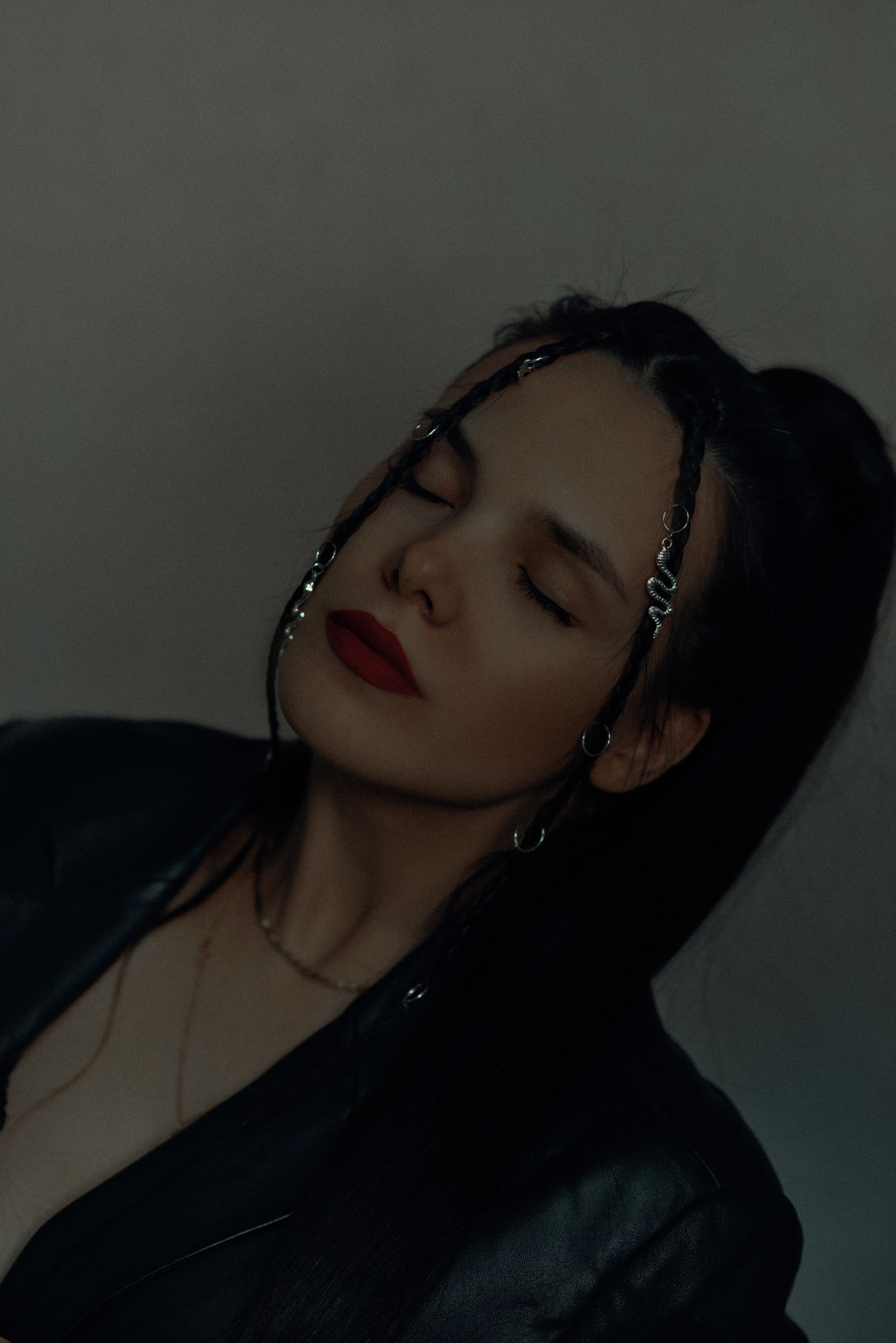 A stylish woman with braided hair and red lipstick poses with eyes closed in a studio setting.