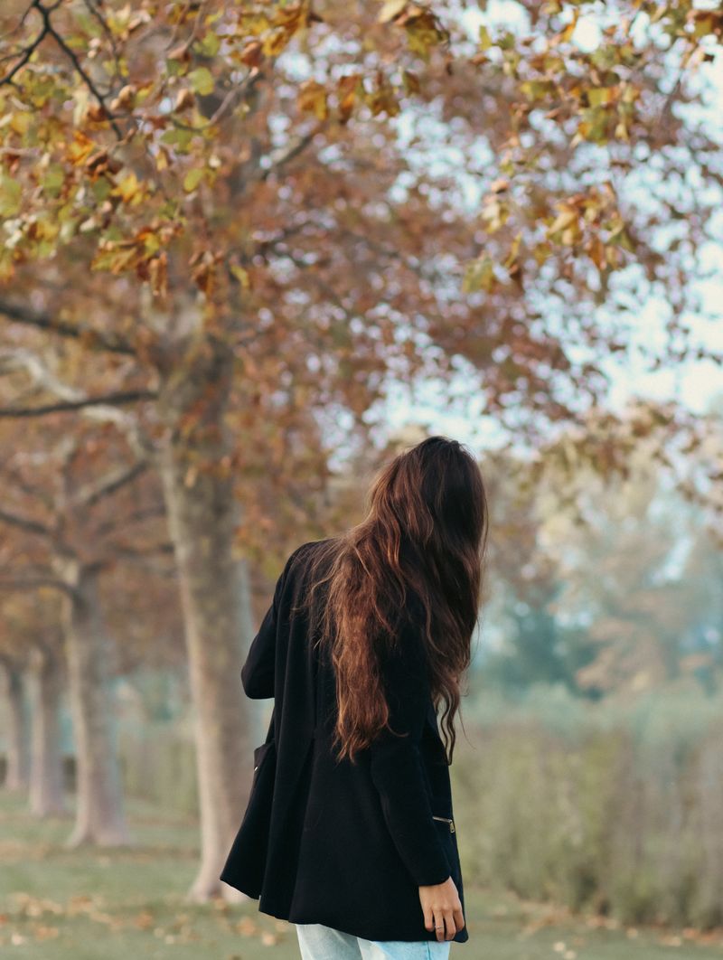 Woman with long dark brown hair walking through an autumn park