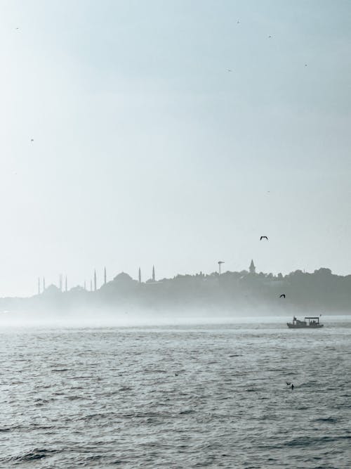 Vintage Boat on a Sea and Coast with Mosques in Mist