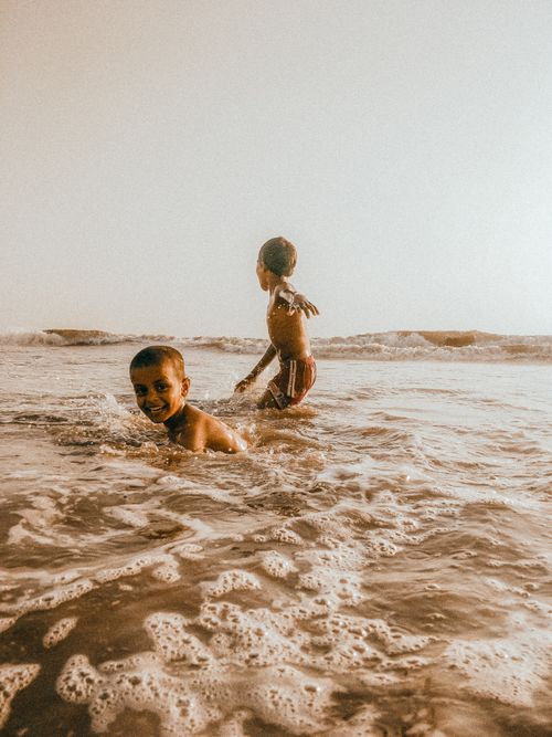 Free Two boys splashing and playing joyfully in the sea waves on a sunny day. Stock Photo