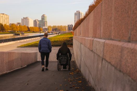 Man and woman in wheelchair walking beside canal in Saint Petersburg in autumn.