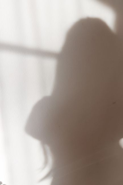 A soft silhouette of a woman is cast against a window, creating a serene and artistic ambiance.