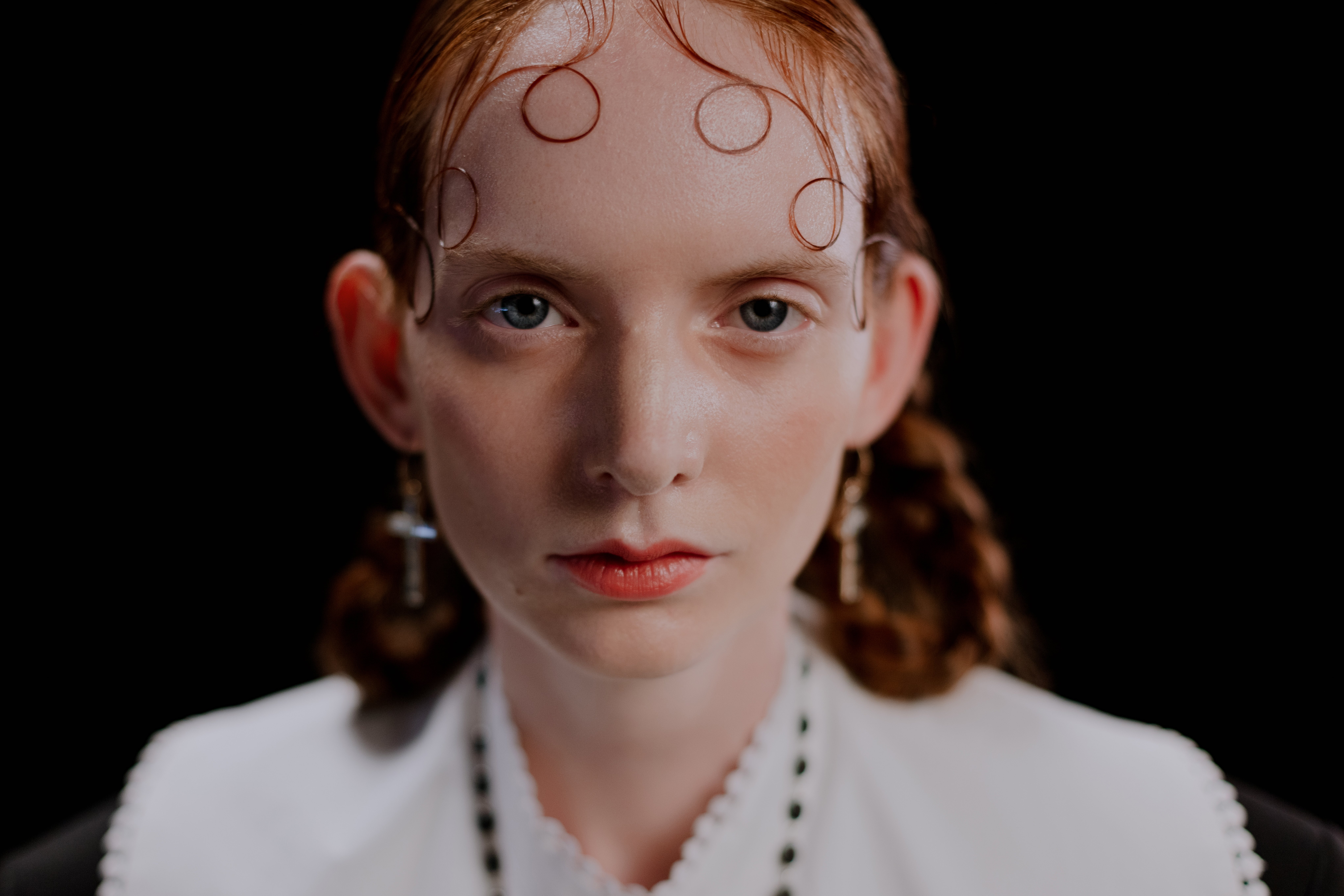 Close-up portrait of a young woman with intricate hairstyle on a black background.