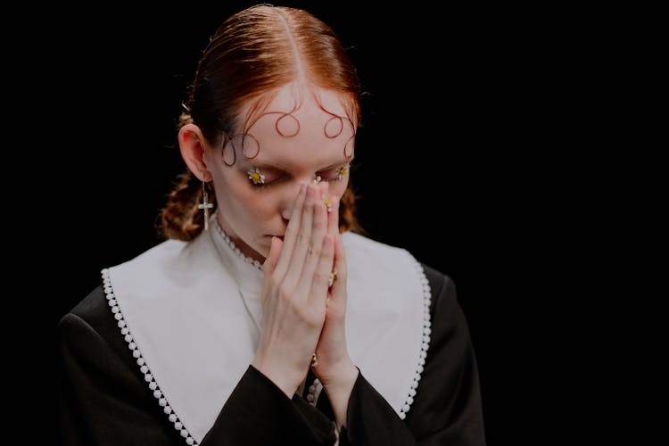 A Woman In Black Long Sleeves Praying Solemnly