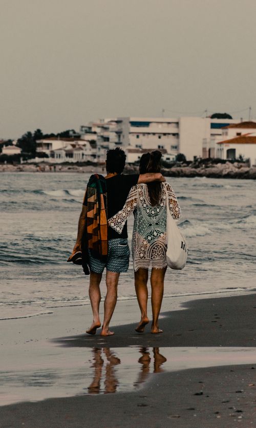 Free A couple enjoys a peaceful stroll along the sandy beach at sunset, capturing a romantic moment. Stock Photo