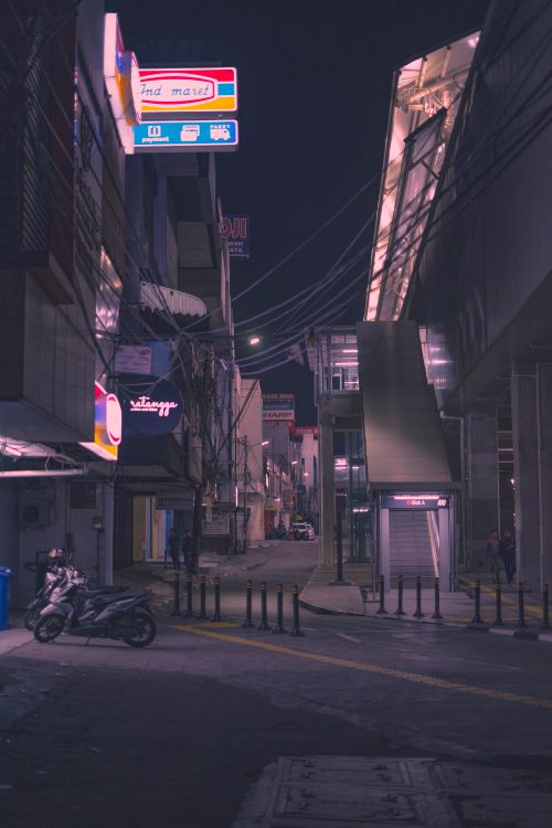 Free A vibrant street at night with neon signage and parked motorcycles, reflecting urban life. Stock Photo