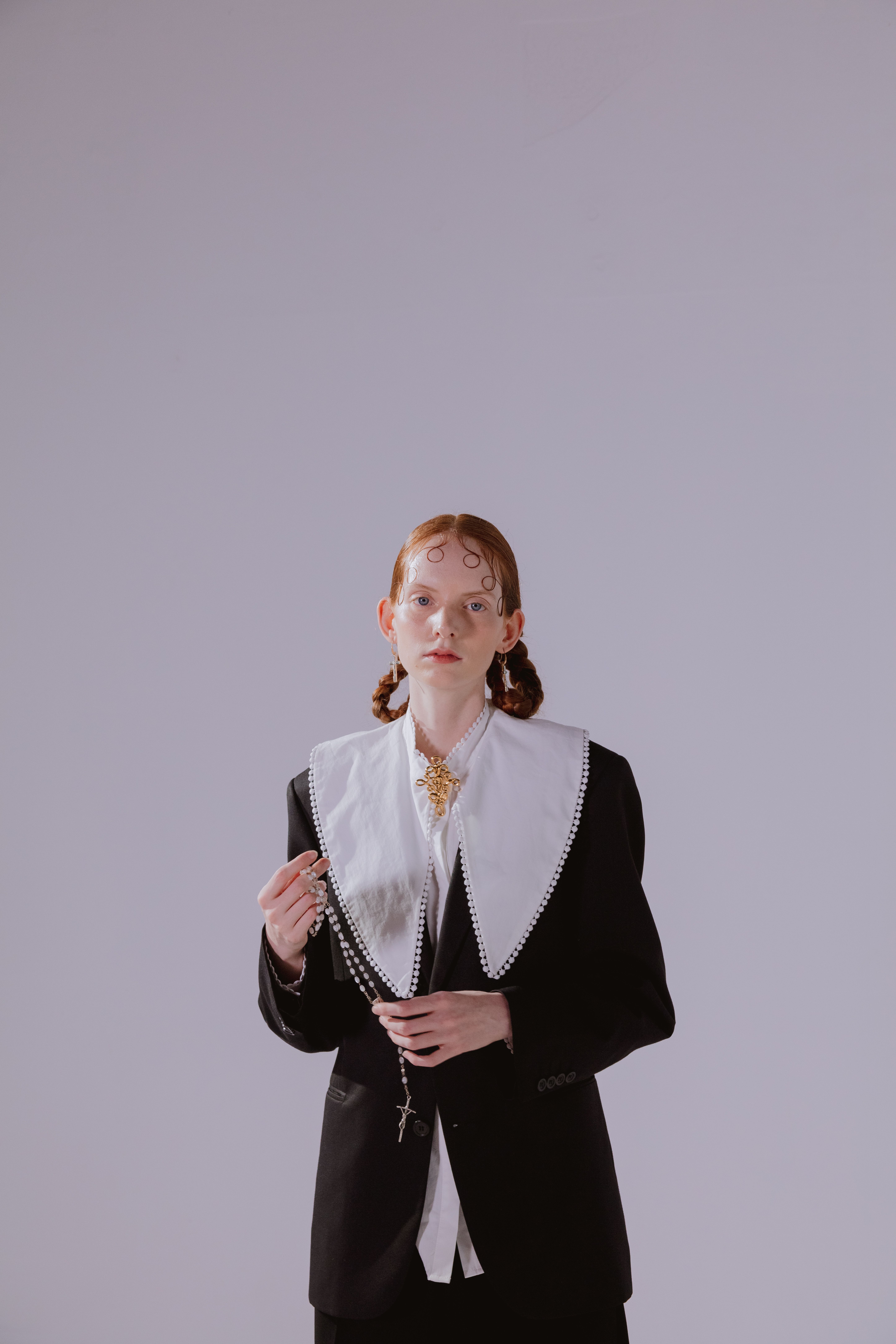 Elegantly dressed woman holding a rosary in a bright studio setting.