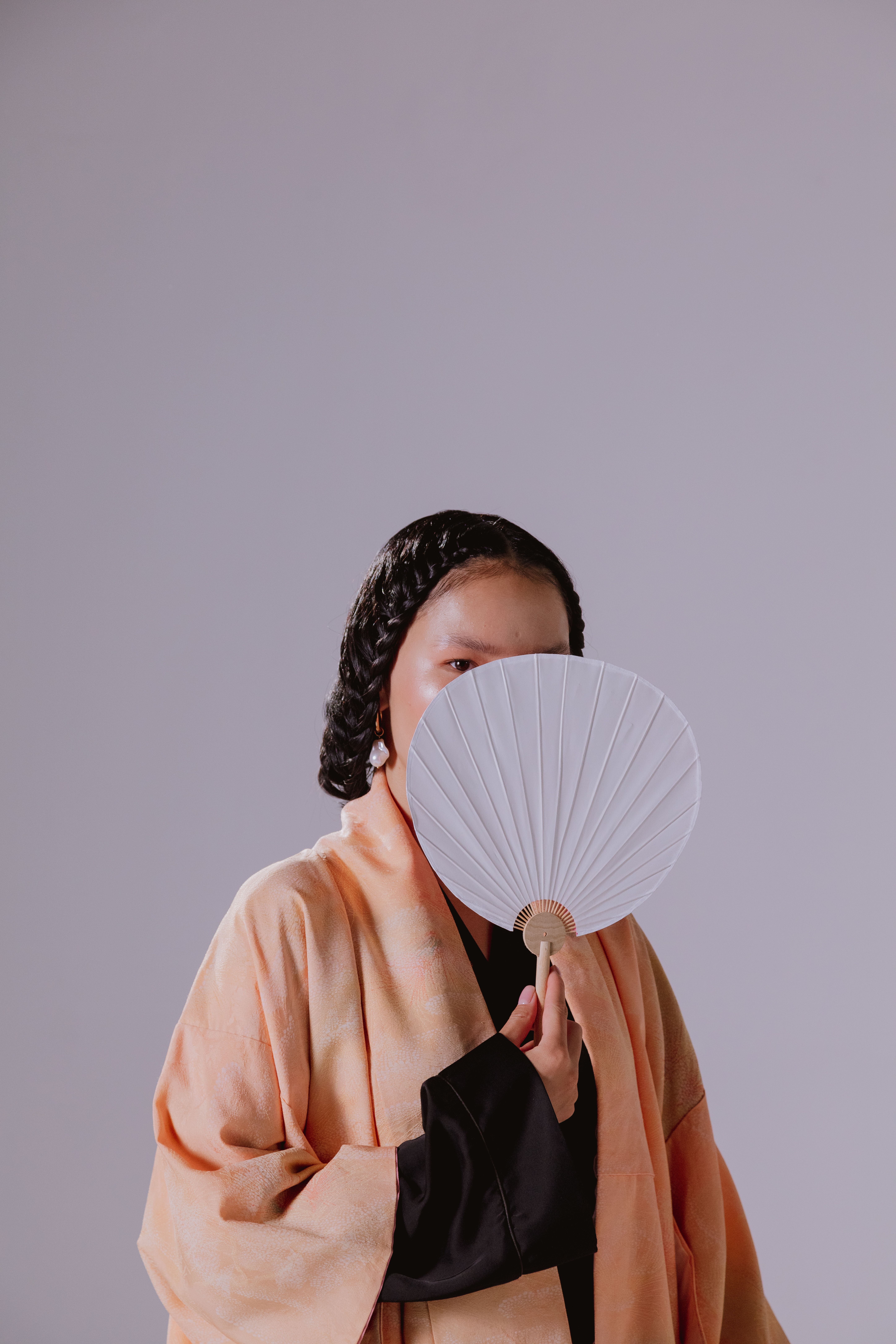 Portrait of a stylish woman in traditional kimono holding a hand fan against a neutral backdrop.