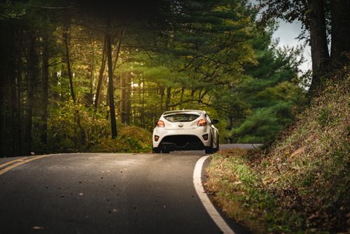 Free Dynamic shot of a white car navigating a winding road through a lush green forest. Stock Photo