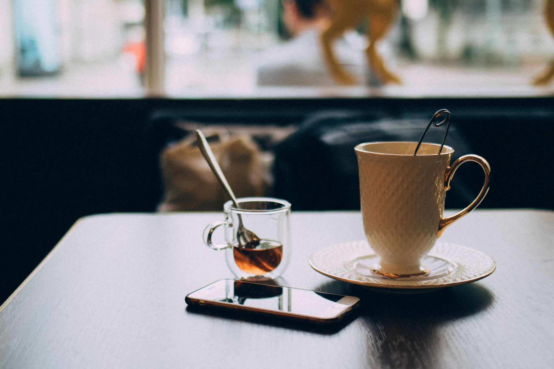 A warm and inviting coffee shop scene featuring a smartphone, tea cup, and small glass of syrup on a table.